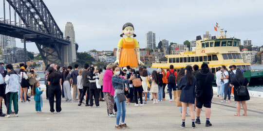 호주 넷플릭스가 지난달 29일부터 이번 달 1일까지 4일간 시드니의 명소 오페라 하우스와 하버 브리지 사이에 '무궁화꽃이 피었습니다' 게임의 술래 '영희' 인형과 분홍색 제복의 진행 요원 등 '오징어 게임' 체험장을 설치해 현지인들의 뜨거운 호응을 받았다. 사진은 1일 호주 시드니하버에 설치된 영희 인형을 찾은 시민들의 모습.   연합뉴스